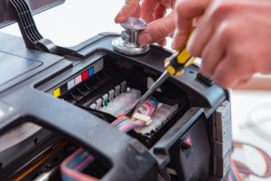 HOW OFTEN SHOULD YOU REPLACE YOUR PRINTER. Man using a screwdriver to help maintain a printer.